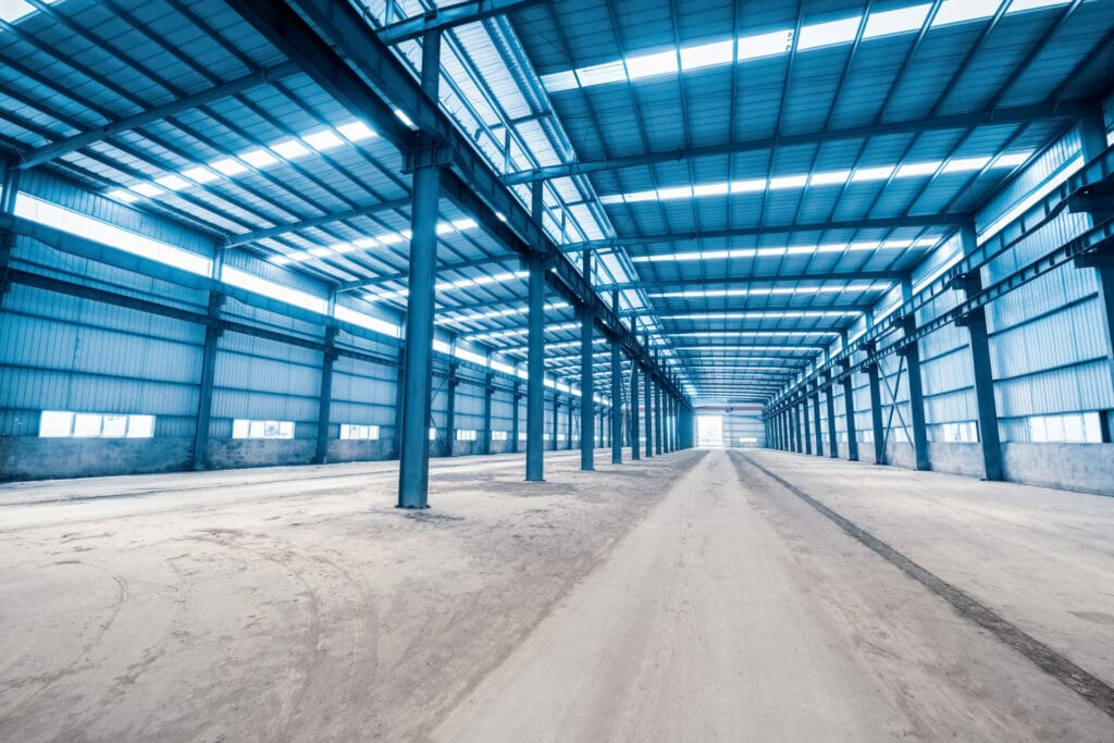 Spacious steel frame warehouse interior with high ceilings and natural light, illustrating modular construction benefits and cost-effective building methods.