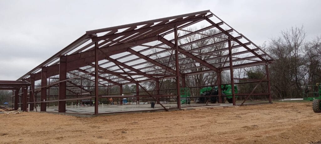 Steel building framework under construction, showcasing structural integrity and compliance with building codes, surrounded by construction equipment and a natural setting.