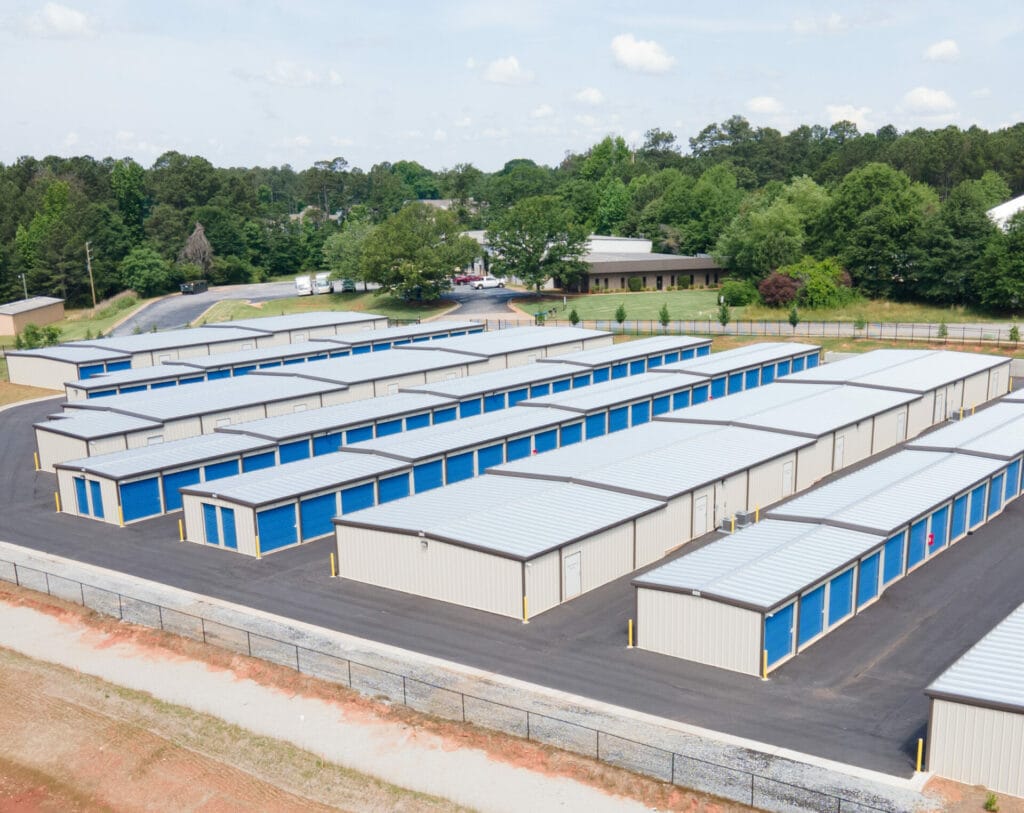 Aerial view of a steel storage facility featuring multiple metal storage units with blue doors, surrounded by greenery and a parking area, illustrating durable construction suitable for varying snow loads and building codes.