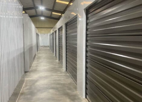 Interior hallway of a climate-controlled storage facility featuring metal storage units with roll-up doors, emphasizing organization and protection for stored items.