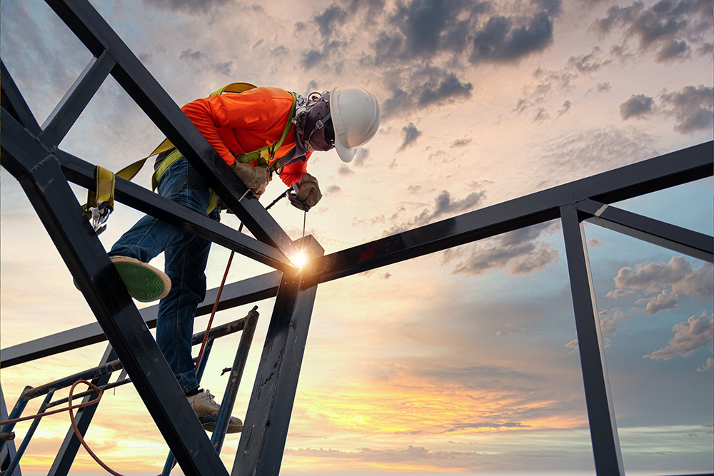 Construction worker welding steel beams at sunset
