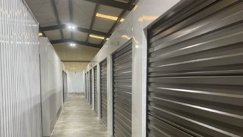 Interior hallway of a climate-controlled storage facility featuring metal storage units with roll-up doors, emphasizing organization and protection for stored items.