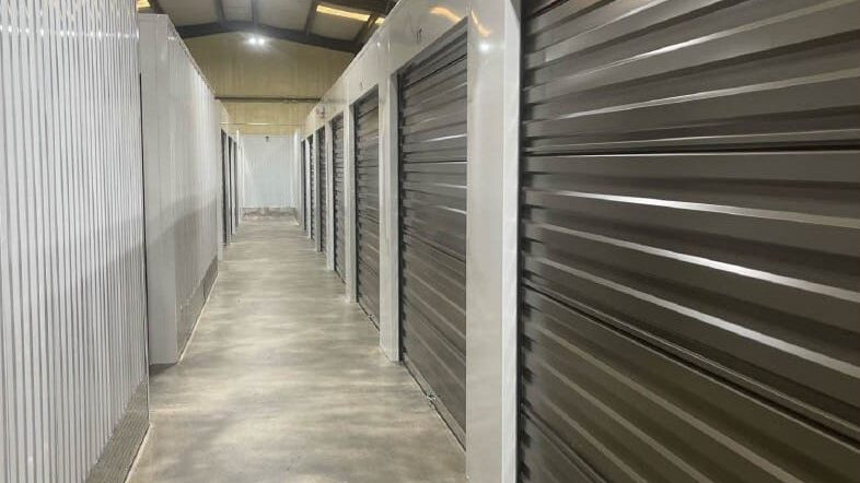 Interior hallway of a climate-controlled storage facility featuring metal storage units with roll-up doors, emphasizing organization and protection for stored items.